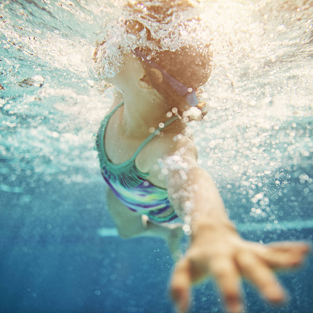 Little girl swimming crawl. Shot from underwater. The girl is reaching towards the camera and taking a breath.