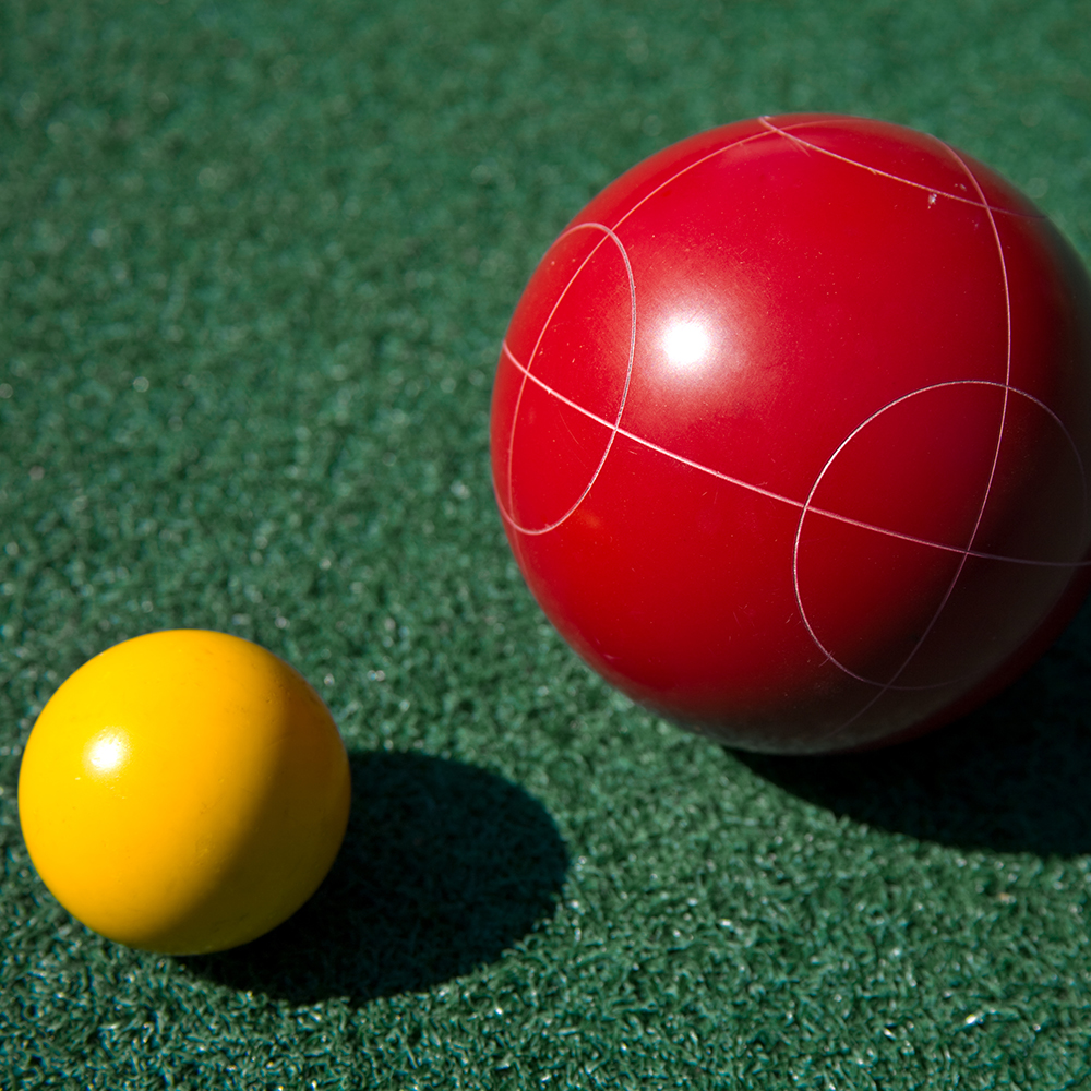 Closeup of a red bocce ball and a yellow palino