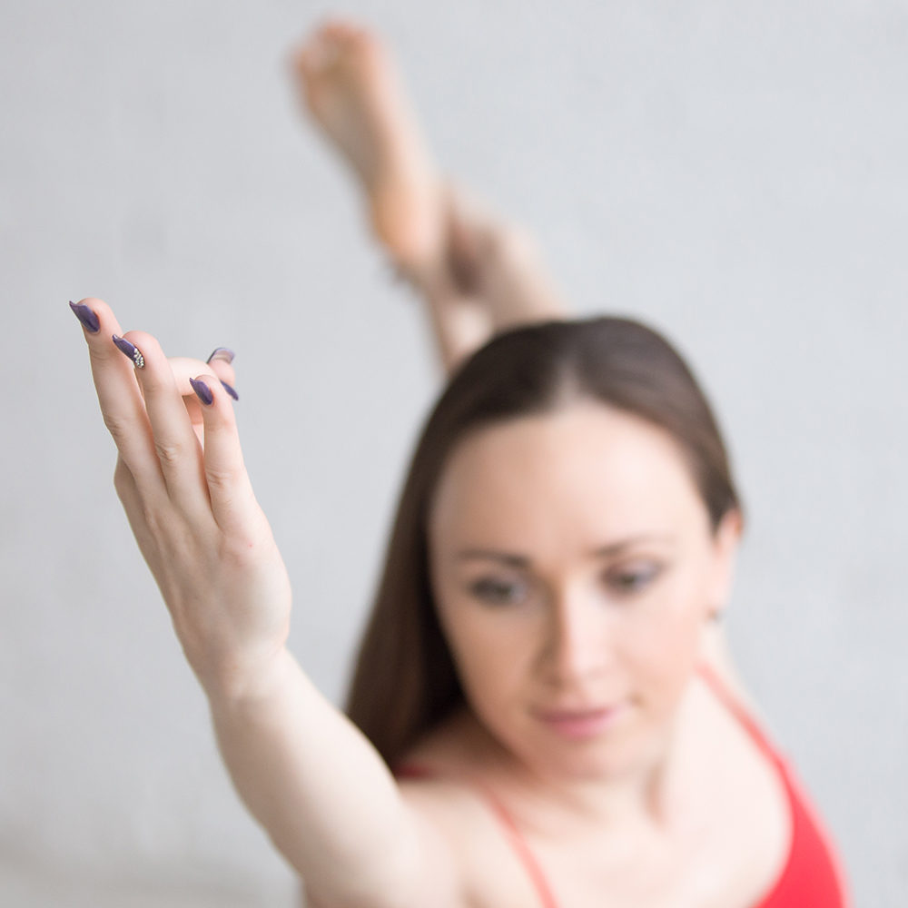 Beautiful young woman in bright colorful sportswear working out indoors in loft interior. Girl standing in Natarajasana Lord of the Dance King Dancer pose. Close-up. Focus on arm