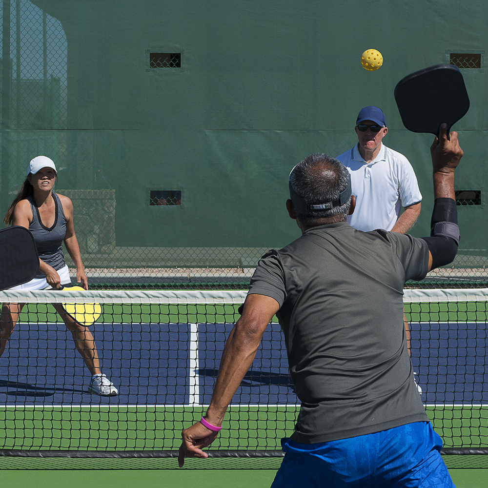 colorful action image of two couples playing a game of pickleball