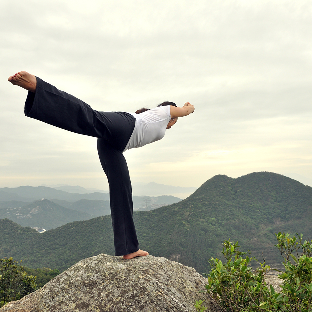 Woman balancing in Warrior III pose on a mountaintop