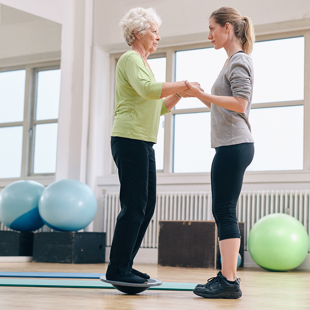 trainer assisting woman on bosu
