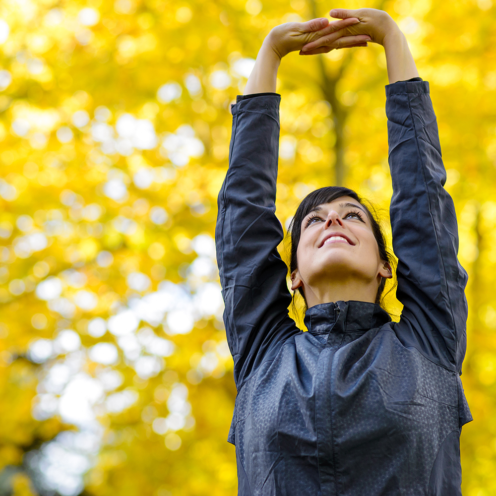 woman stretching arms overhead in yellow leaves