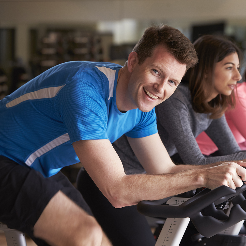 Man in a spinning class at a gym turning to smile at camera