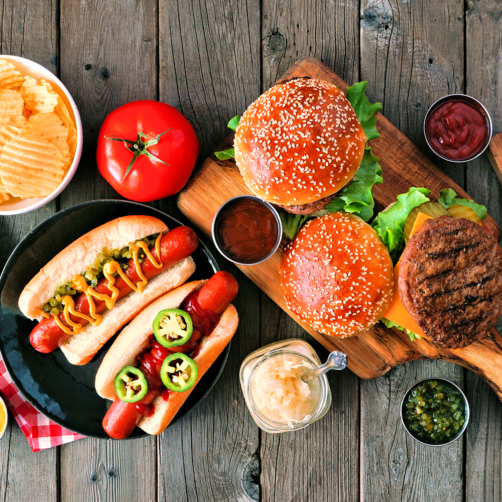 Summer BBQ food table scene with hot dog and hamburger buffet. Above view over a rustic wood background.