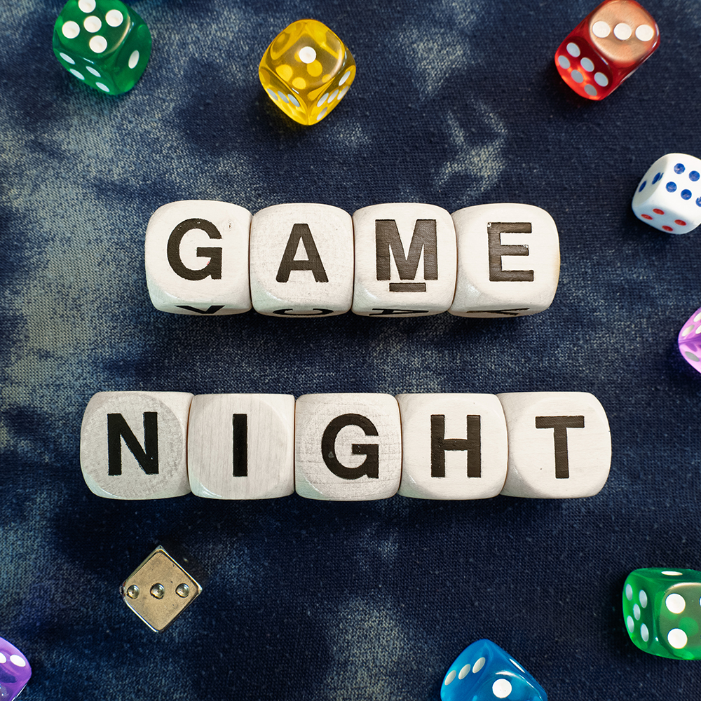 GAME NIGHT spelt using wooden word dice with vibrant dice around set over a swrily blur fabric background - perfect for promoting game events or fun family gatherings.